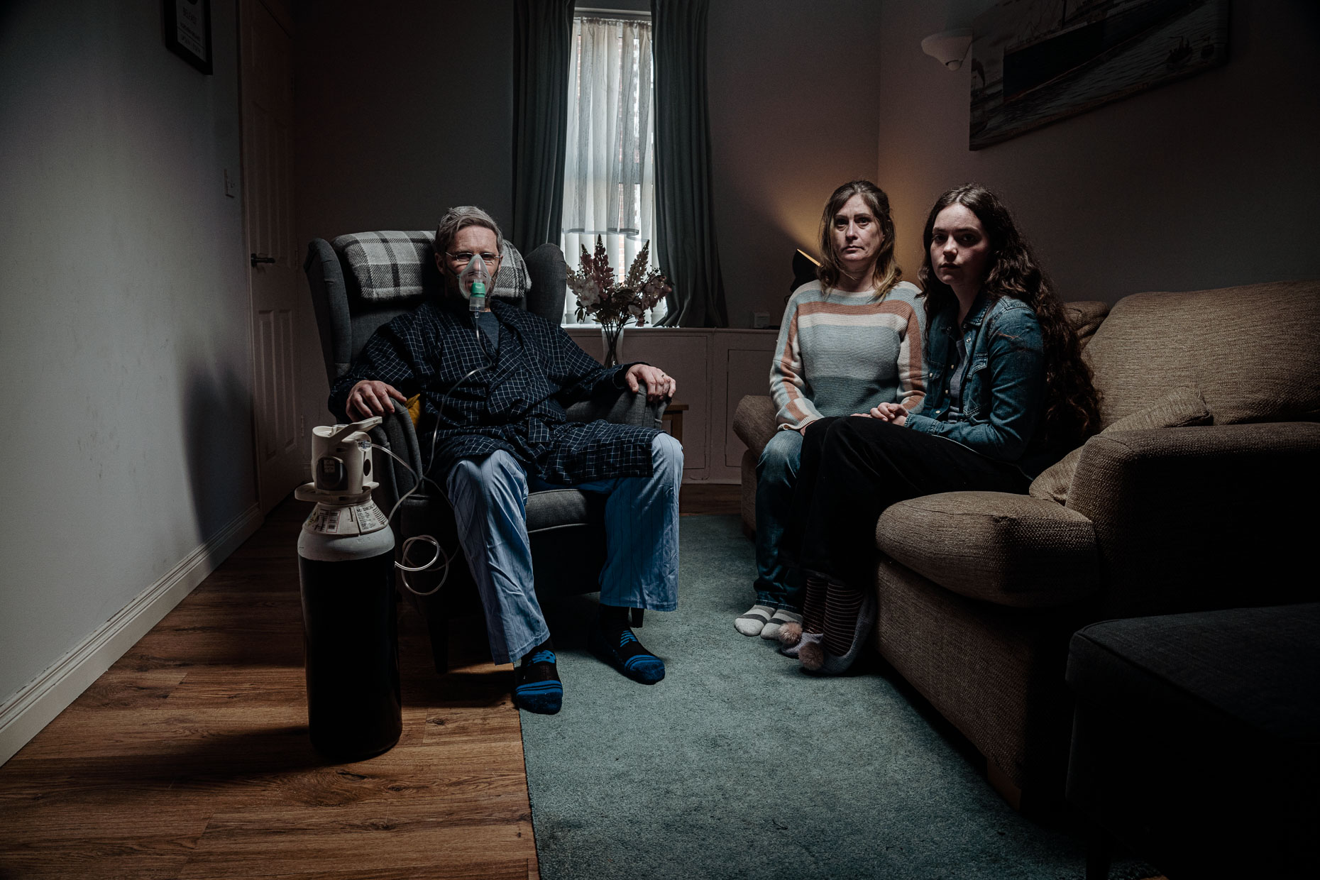 A family sits in the living while the dad breaths with an oxygen tank
